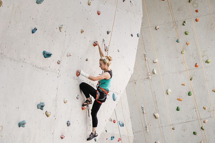 Eine junge Frau klettert an einer Kletterwand empor.