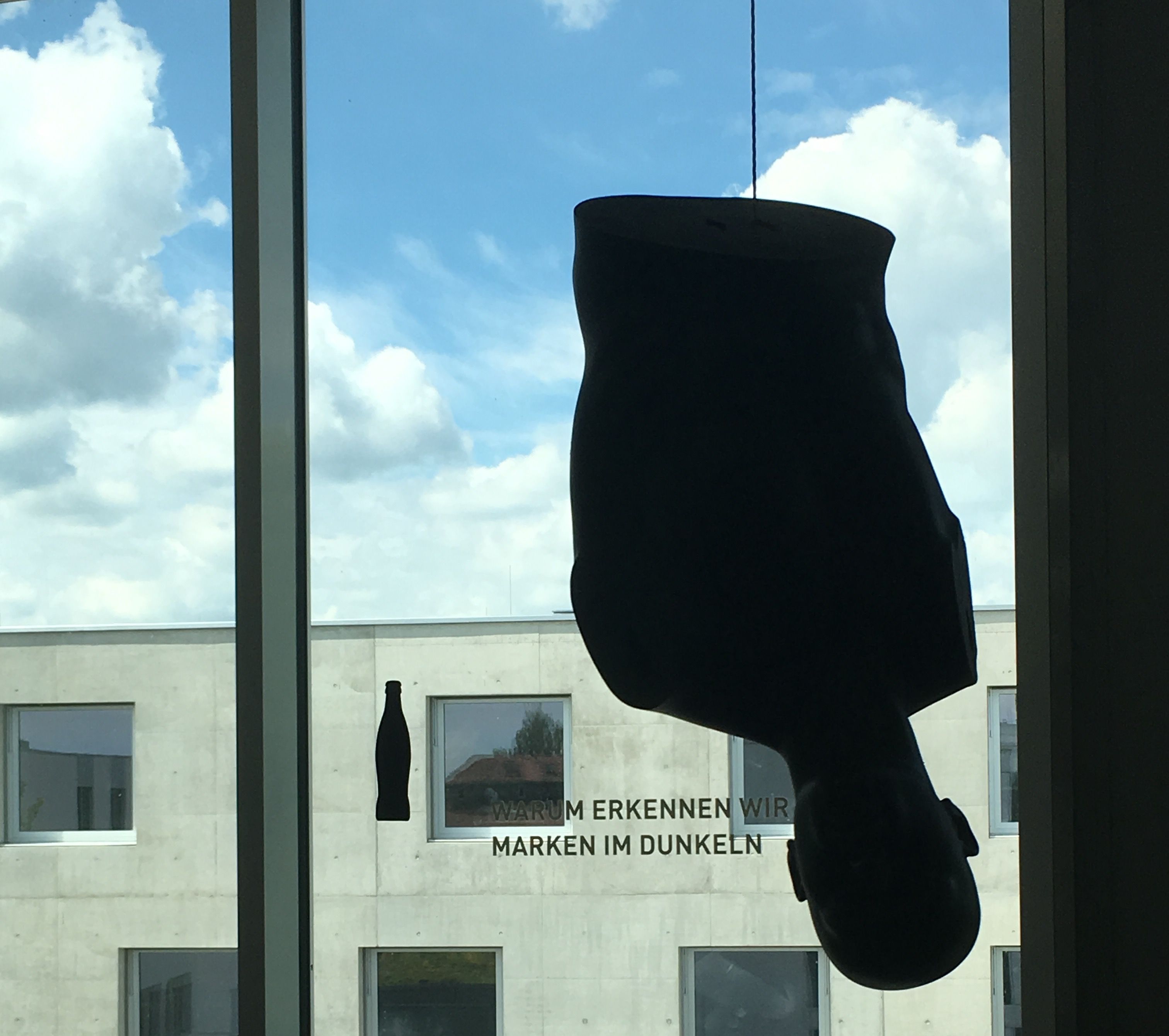 Der Torso einer Schaufensterpuppe hängt mit dem Kopf nach unten vor einem Fenster im L-Gebäude