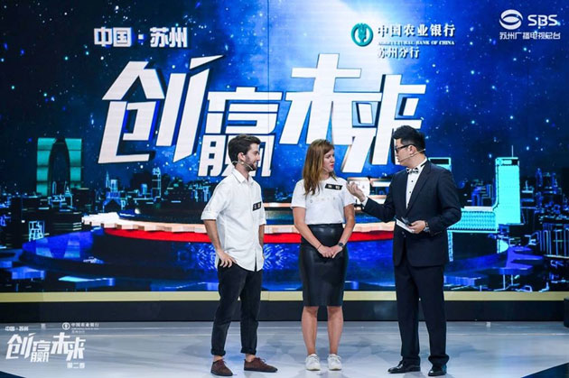 Marcel Münch (links) und Miriam Theobald (Mitte) stehen mit einem chinesischen Moderator auf der Bühne einer Fernsehshow. Im Hintergrund sind chinesische Schriftzeichen zu sehen. 