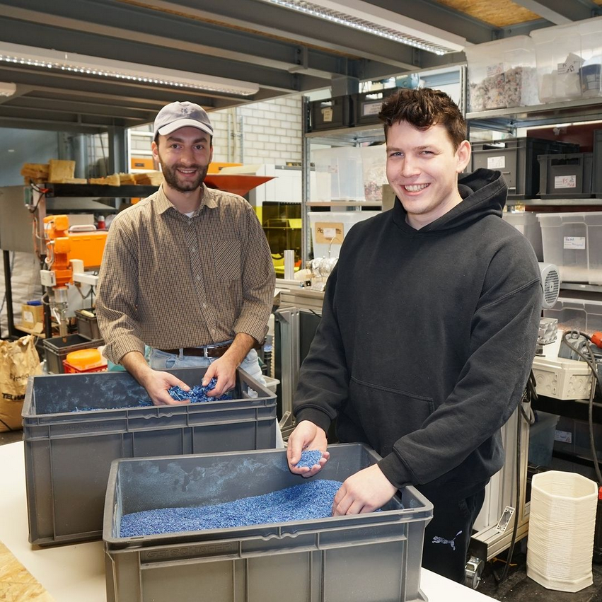 Zwei Studierende im Open Innovation Lab mit den Händen in zwei Kisten mit geschreddertem Plastik.