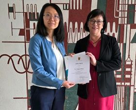 Zwei Frauen stehen vor der Kamera und halten eine Urkunde in den Händen