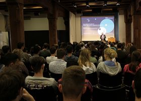 Prof. Dr. Erdal Yalcin von der HTWG steht auf einer Bühne im Konzilgebäude und hält bei der Veranstaltung Economics Goes School einen Vortrag vor vielen Schüler*innen.