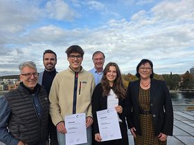 Vier Männer und zwei Frauen lächeln auf einer Dachterasse in die Kamera