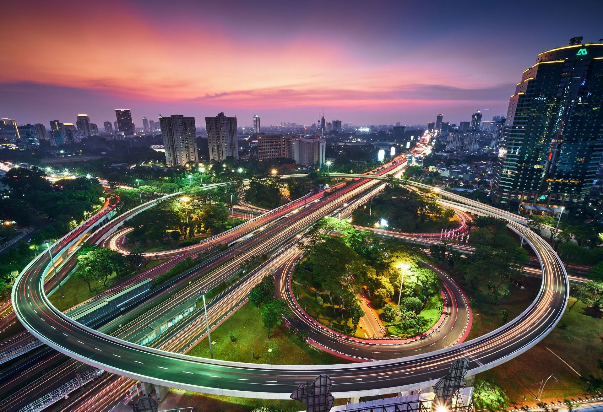 Stadtbild Jakarta/Indonesien aus der Vogelperspektive: Abendstimmung mit rot-violettem Himmel, glitzerndes Straßennetz und Gebäuden. 