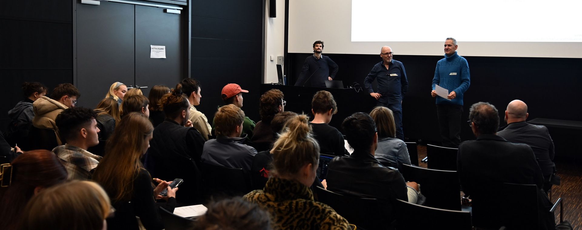 Foto des Vortragssaals von hinten mit Publikum und Referenten