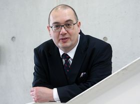 Ein Mann in Anzug mit Krawatte lehnt an einer Treooebvrstung
