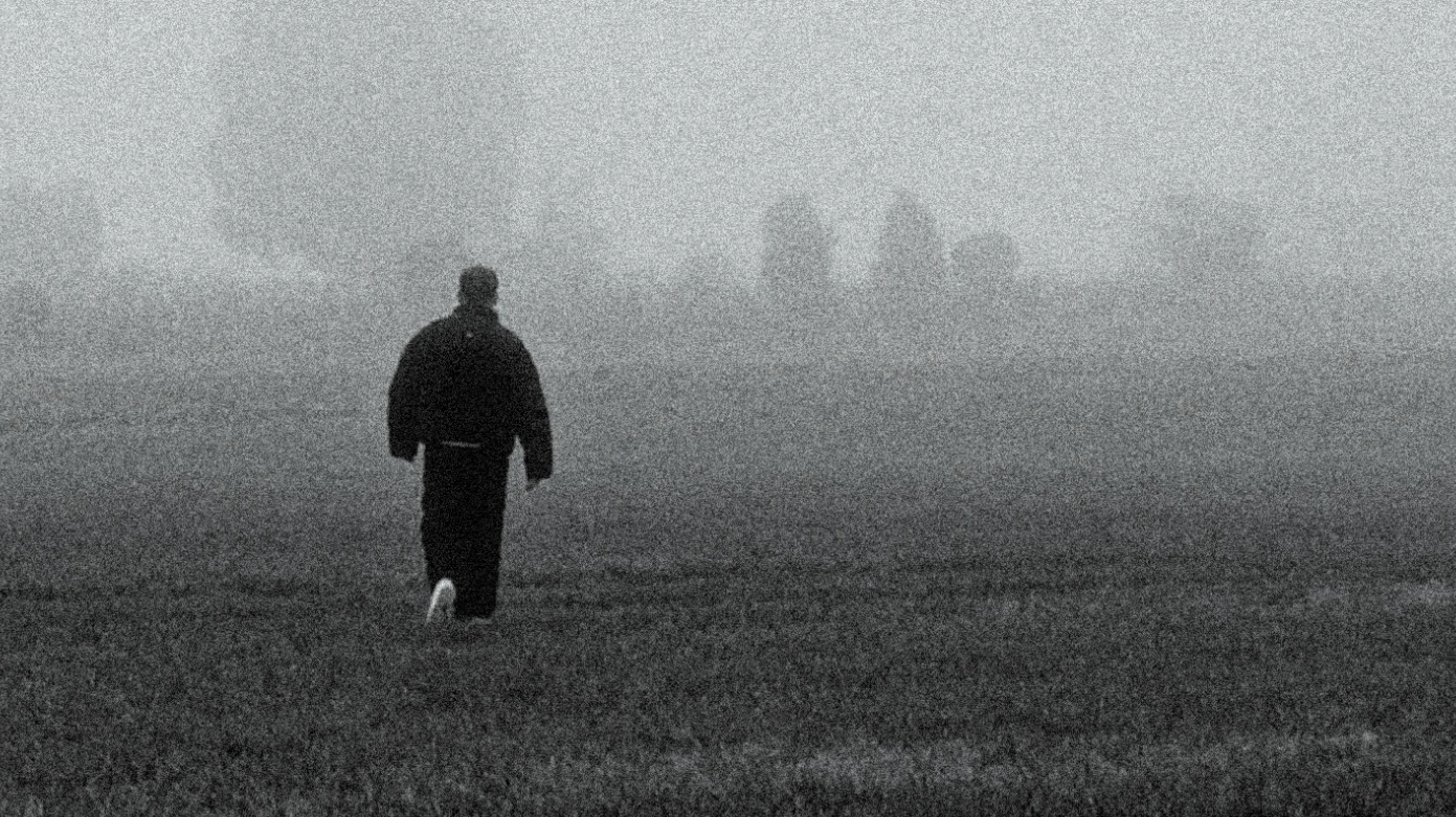 Schwarz-weiß Foto, das eine Person von hinten zeigt, die über eine Wiese geht