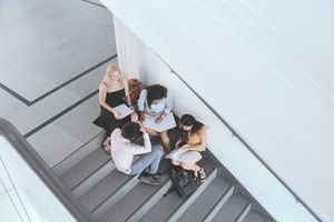 4 Studierende sitzen auf einer Treppe im Gebäude und erarbeiten sich ein Thema