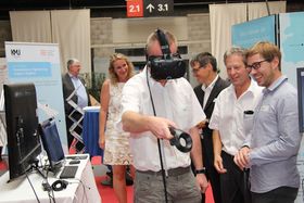 Menschen an einem Messestand. Im Vordergrund ein Mann, der eine VR-Brille trägt.