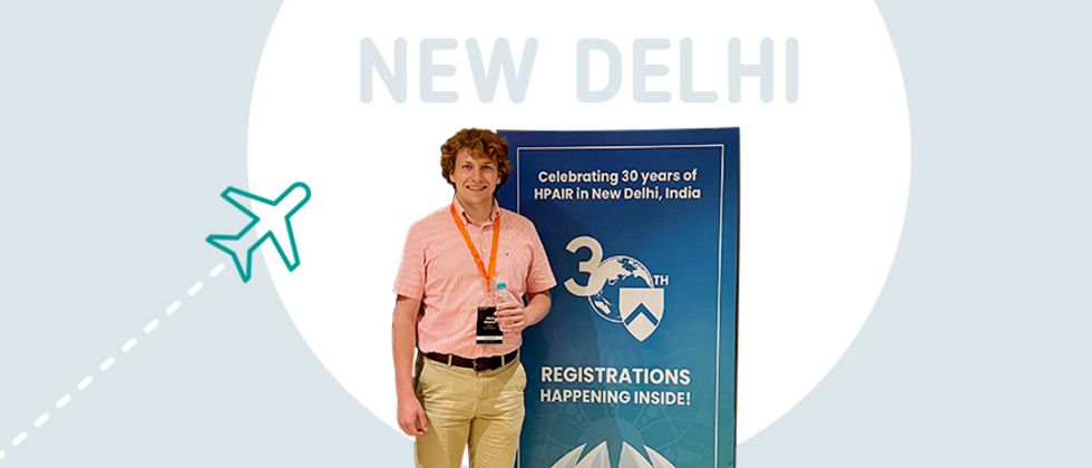 HTWG-Student Jakob Nischan steht neben einem Aufsteller der HPAIR in Neu Delhi, zu der er mit einem Reisestipendium anreiste.