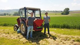 Kleiner Traktor auf einem Feld mit zwei Studierenden am hinten angebrachten Mikrogranulatstreuer