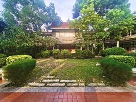 Ein schöner grüner Gartenbereich mit grünen Büschen und Bäumen vor einem kleinen hellen Häuschen mit rotem Ziegeldach, welches zum Campus of European and Asian Languages der Wenzao Ursuline University gehört. 