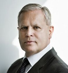 Roland Steinmeyer steht vor einem hellen Hintergrund, trägt einen dunklen Anzug mit dunkler Krawatte und hat kurze Haare.