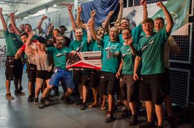 Eine Gruppe junger Menschen in grünen T-Shirts posieren fürs Foto. Sie recken die Fäuste in die Luft und Jubeln. Ein junger mann hält ein Plakat mit der Aufrschift "MotoStudent" in der Hand. Ein weiterer reckt einen Pokal in die Luft.