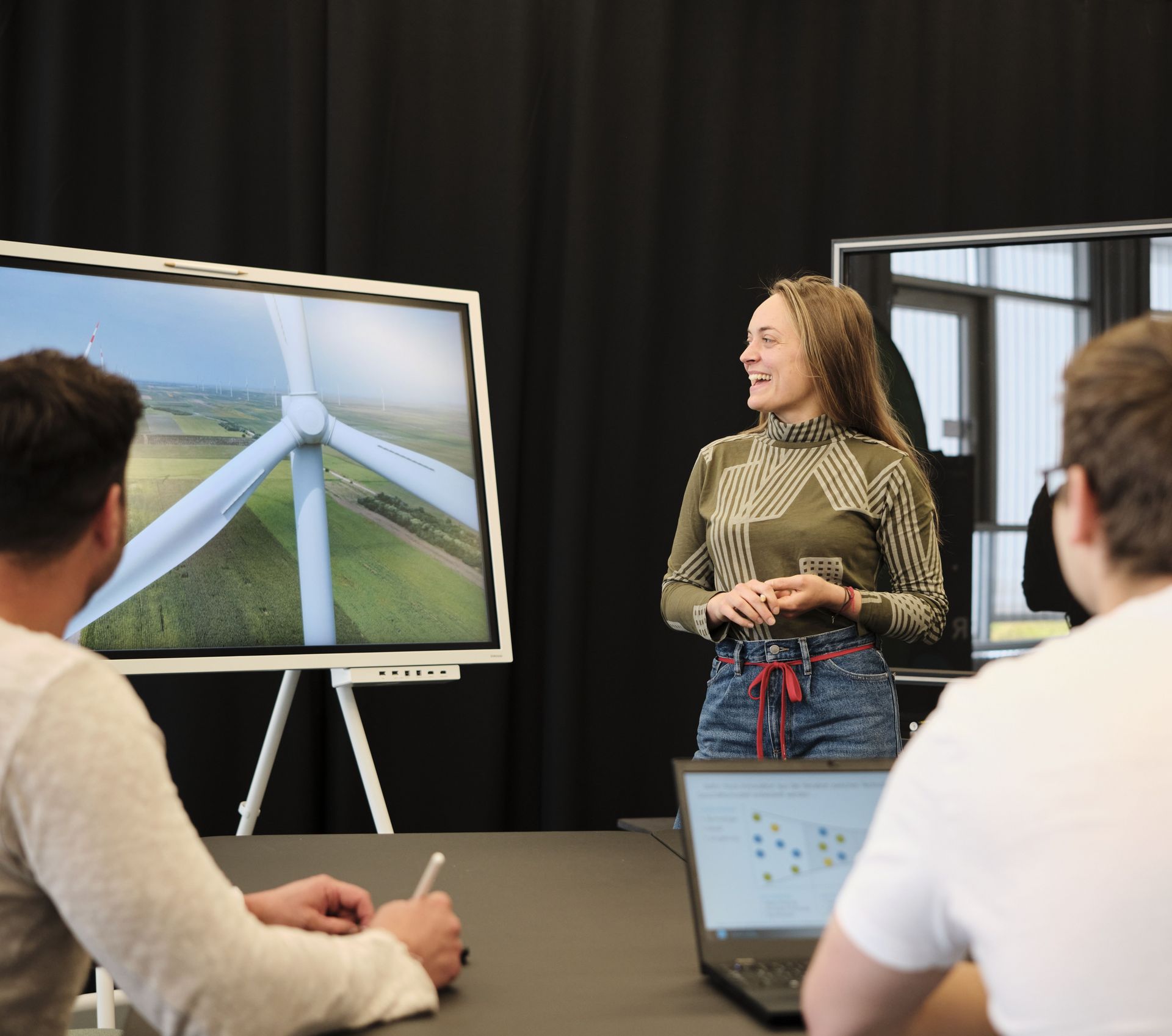 Eine Studentin hält einen Vortrag über Winkraftanlagen mit einem smarten Whiteboard vor zwei Studenten an einem Gruppentisch Eine Studentin hält einen Vortrag über Winkraftanlagen mit einem smarten Whiteboard vor zwei Studenten an einem Gruppentisch