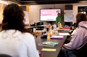 Zu sehen ist ein Seminarraum. Im Vordergrund steht Sandra Flügel an einem Bildschirm, sie präsentiert das BEST-Training. Schüler hören aufmerksam zu.