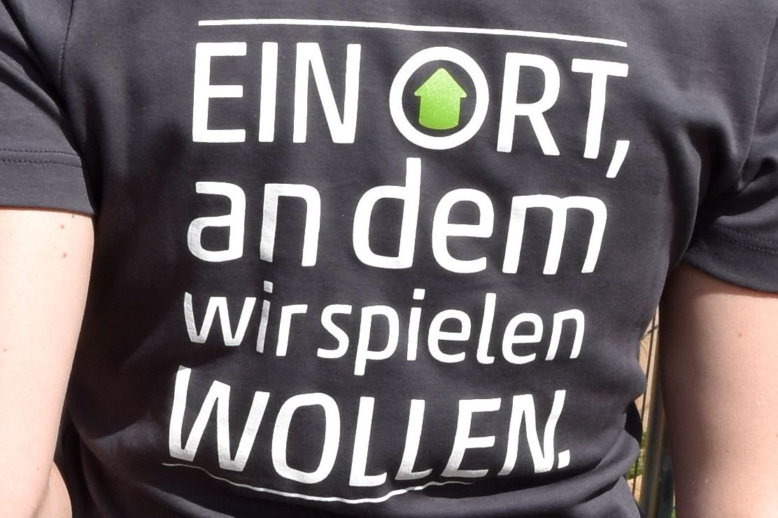 T-Shirt auf dem "Ein Ort an dem wir spielen wollen." steht.