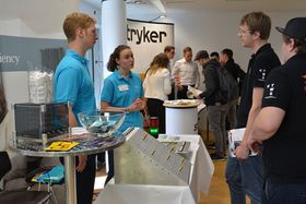 Ein Messestand: Eine junge Frau und ein junger Mann sprechen mit zwei Besuchern in T-Shirts mit HTWG-Logo auf dem Ärmel.