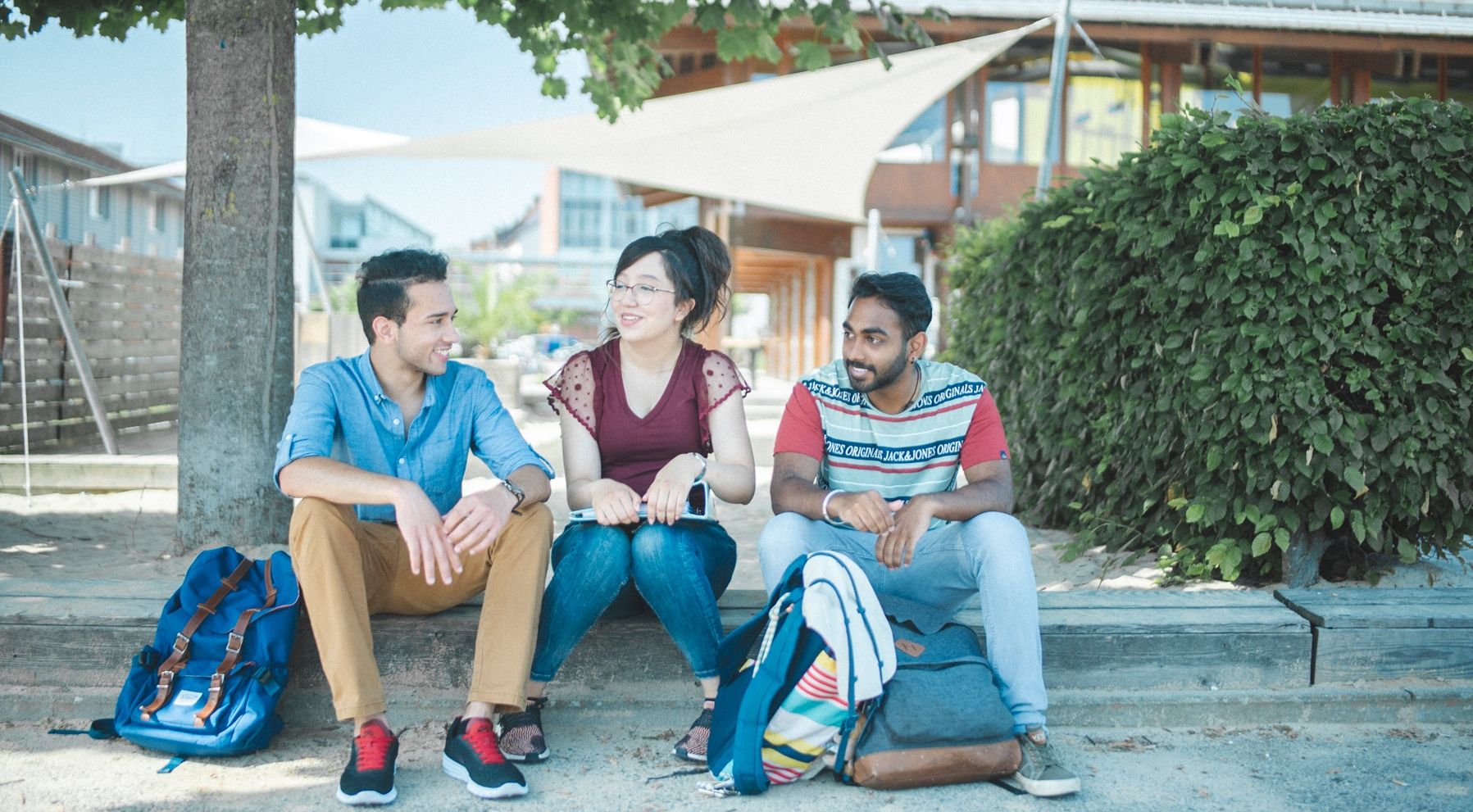 Drei internationale Studierende sitzen vor der HTWG Mensa.