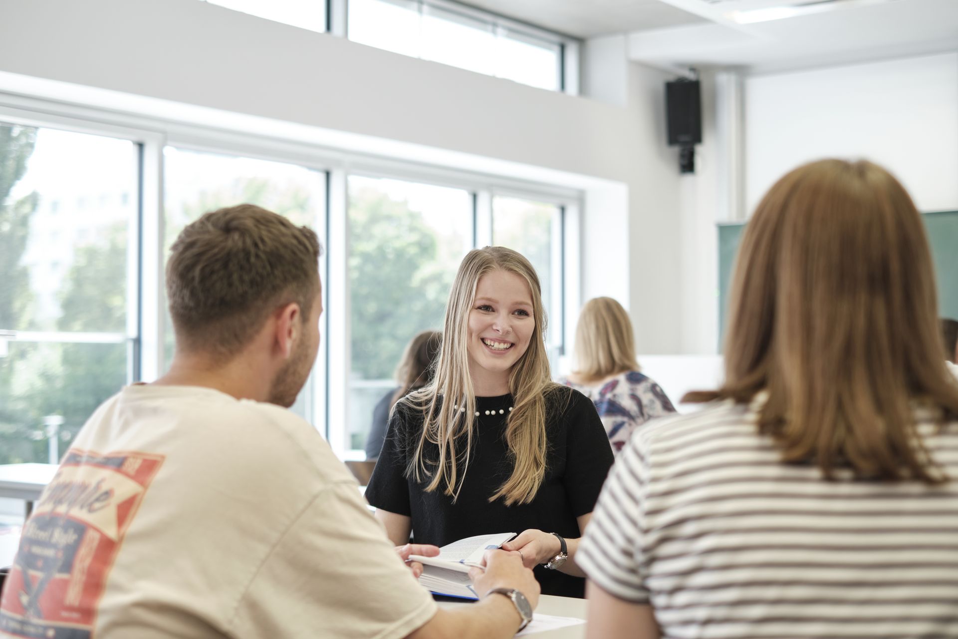 Drei Studierende sitzen an einem Tisch und sprechen miteinander.