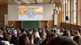 Studierende sitzen in einer Aula und schauen eine Präsentation an