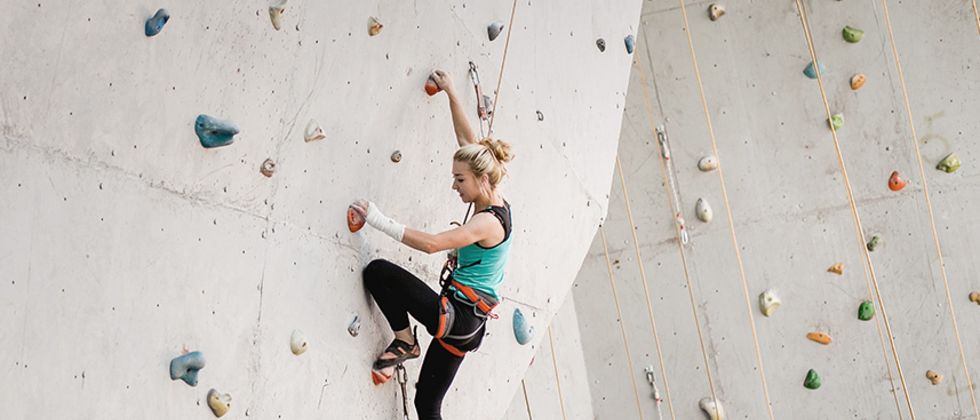 Eine junge Frau klettert an einer Kletterwand empor.