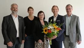 Gruppenbild des Präsidiums (2 Frauen und 2 Männer) in schicker Kleidung vor einer weißen Wand. Einer der Männer hält einen Blumenstrauß.