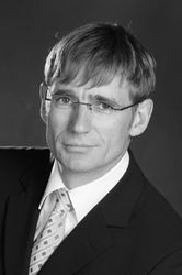 Schwarz-Weiß-Bild von Maximilian Jantz im Anzug mit Krawatte. Er hat die Haare in die Stirn gekämmt und trägt eine Brille.