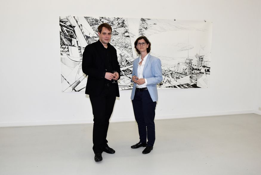 Robert Patz (links) und Prof. Katrin Günther (rechts) stehen in einem Ausstellungsraum vor einer Zeichnung von Katrin Günther.