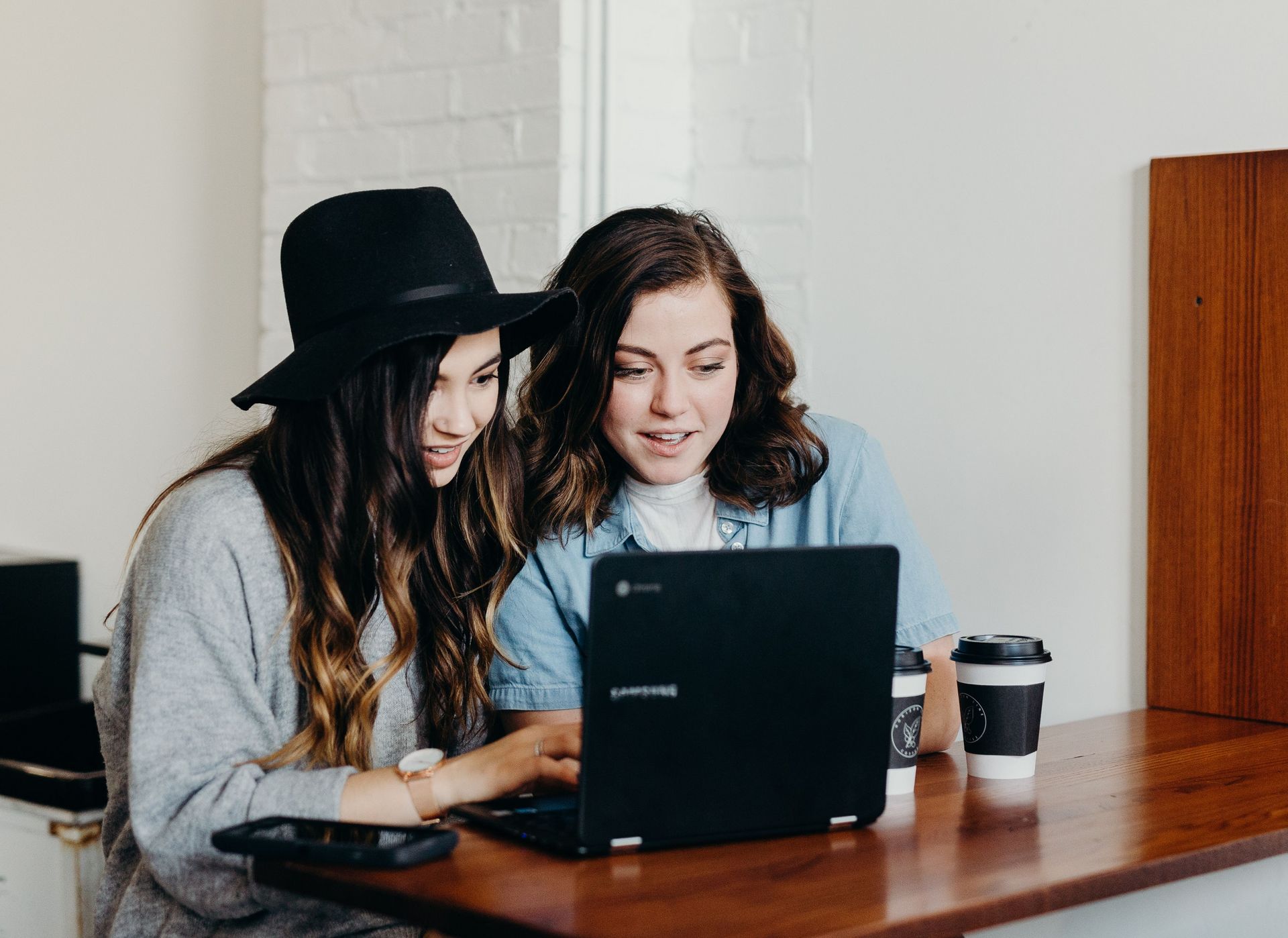 Zwei junge Frauen sitzen vor einem Laptop und unterhalten sich