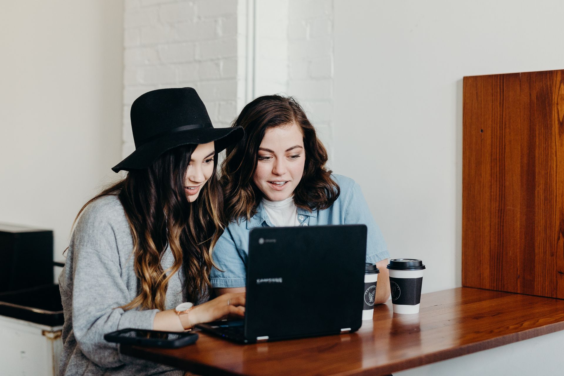 Zwei junge Frauen sitzen vor einem Laptop und unterhalten sich