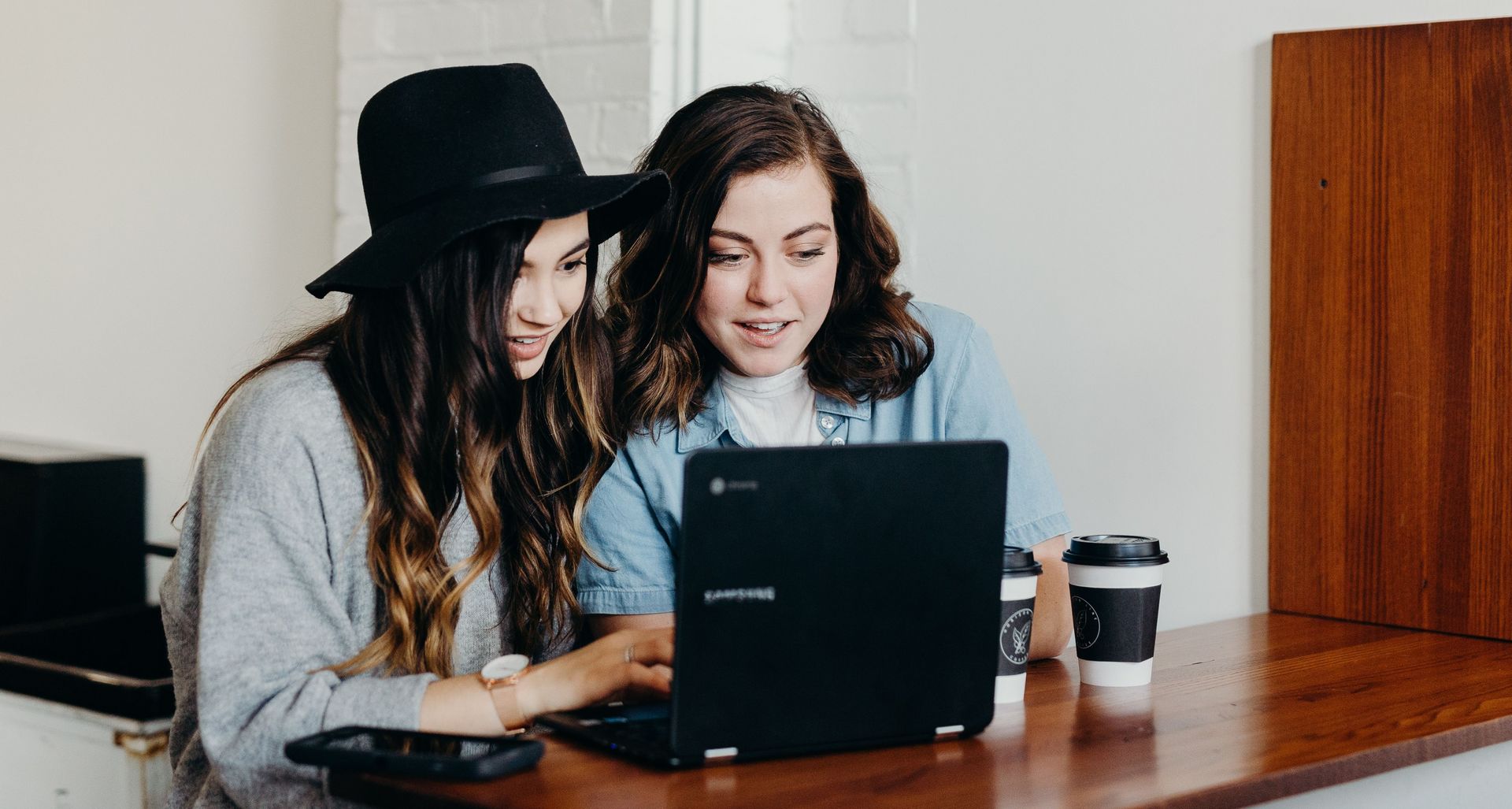 Zwei junge Frauen sitzen vor einem Laptop und unterhalten sich