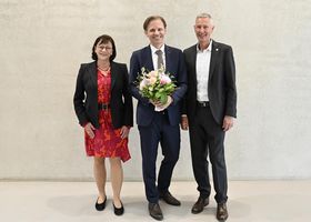 Eine Frau und zwei Männer lächeln freudig in die Kamera