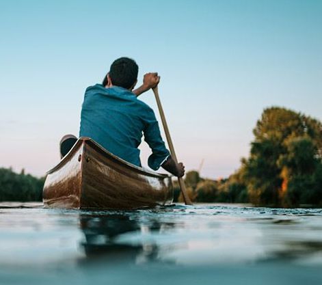 A young man paddling into the sunset on a river