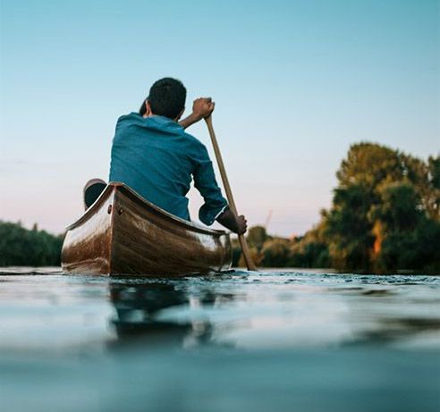 Ein junger Mann paddelt auf dem Wasser Richtung Sonnenuntergang