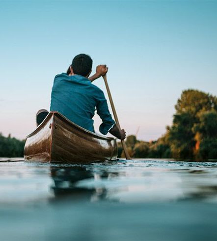 Ein junger Mann paddelt auf dem Wasser Richtung Sonnenuntergang