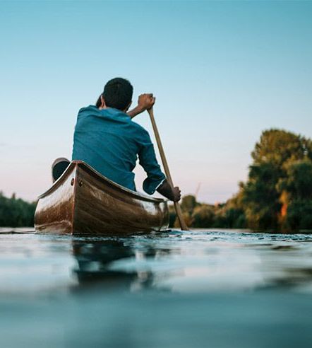 A young man paddling into the sunset on a river