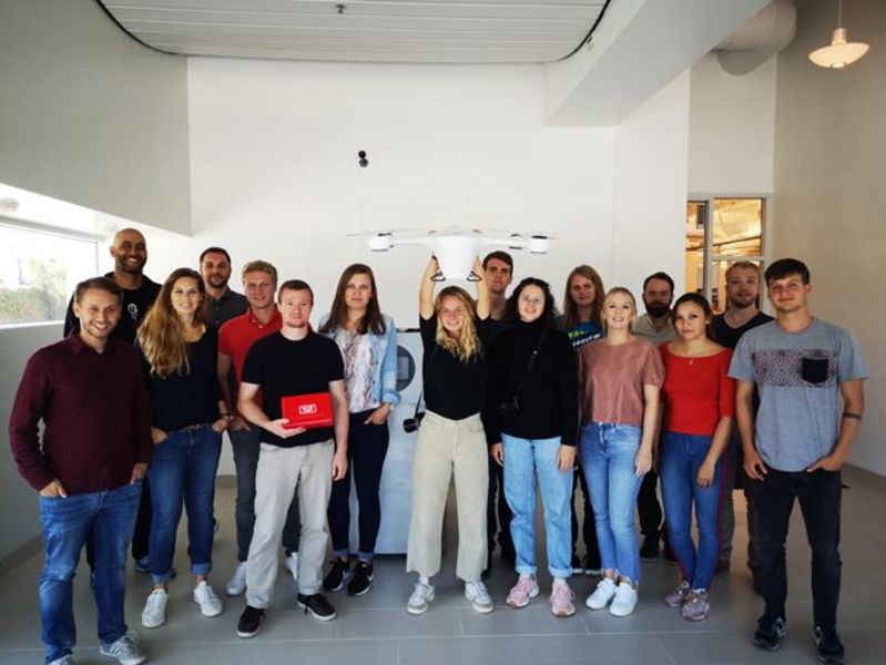 Gruppenfoto: Zirka 30 junge Menschen stehen vor einer weißen Wand und lachen in Richtung des Fotografen.