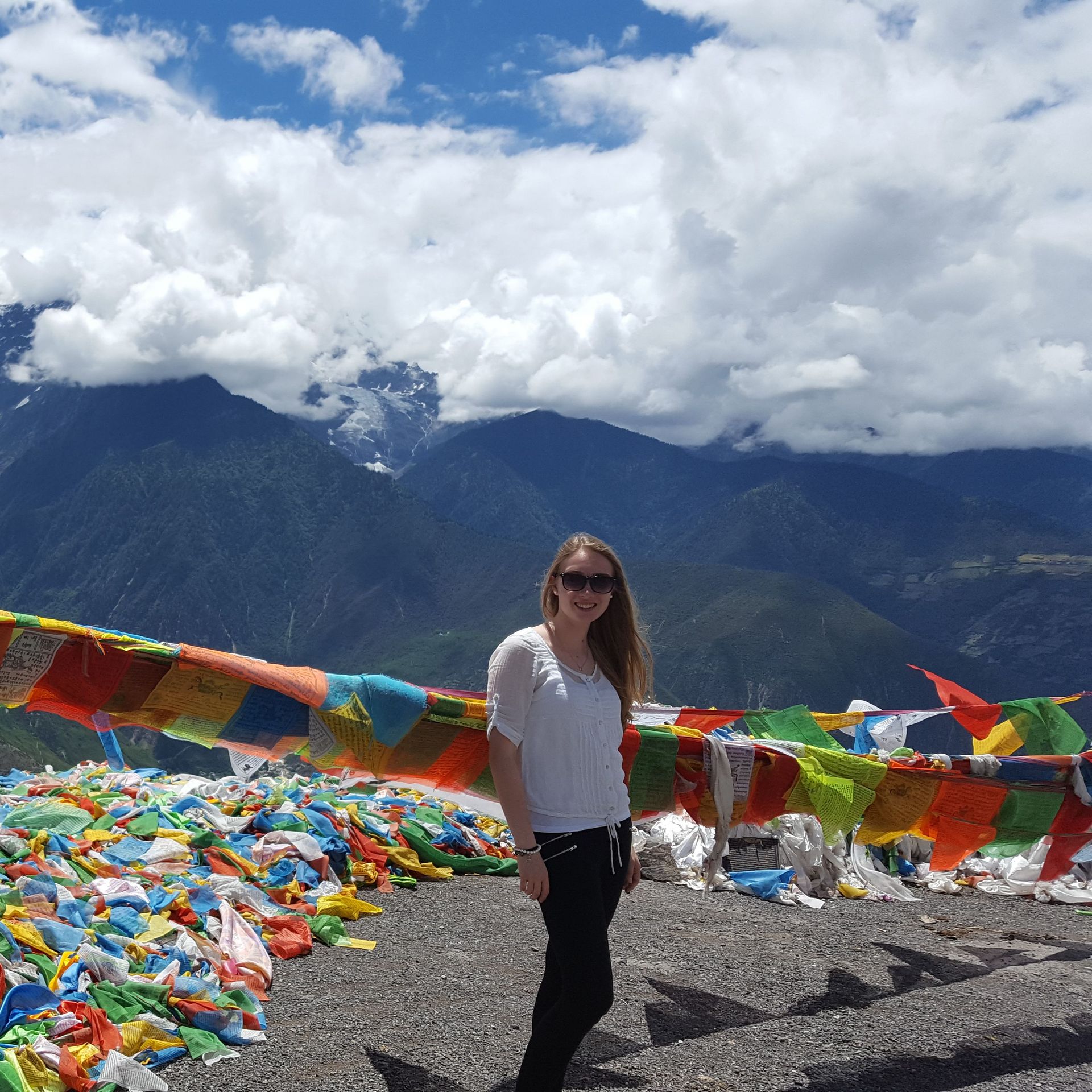 A photograph showing former student Valerie Ehlebracht in front of a beautiful mountain landscape with multi-colored Tibetan flags