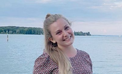 Eine junge Frau steht am Bodensee und lächelt in die Kamera