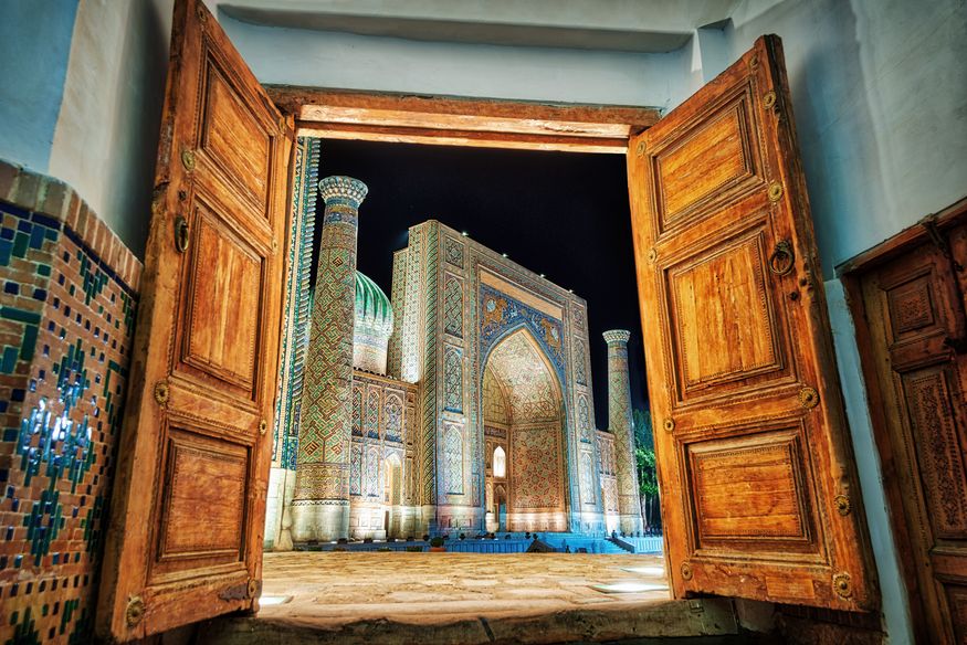 Blick durch ein Holztoor auf ein mit bunten Mosaiksteinchen geschmücktes Portal
