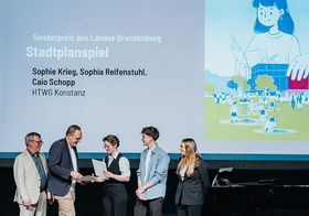 2 Männer verleihen drei Studierenden auf einer Bühne eine Urkunde