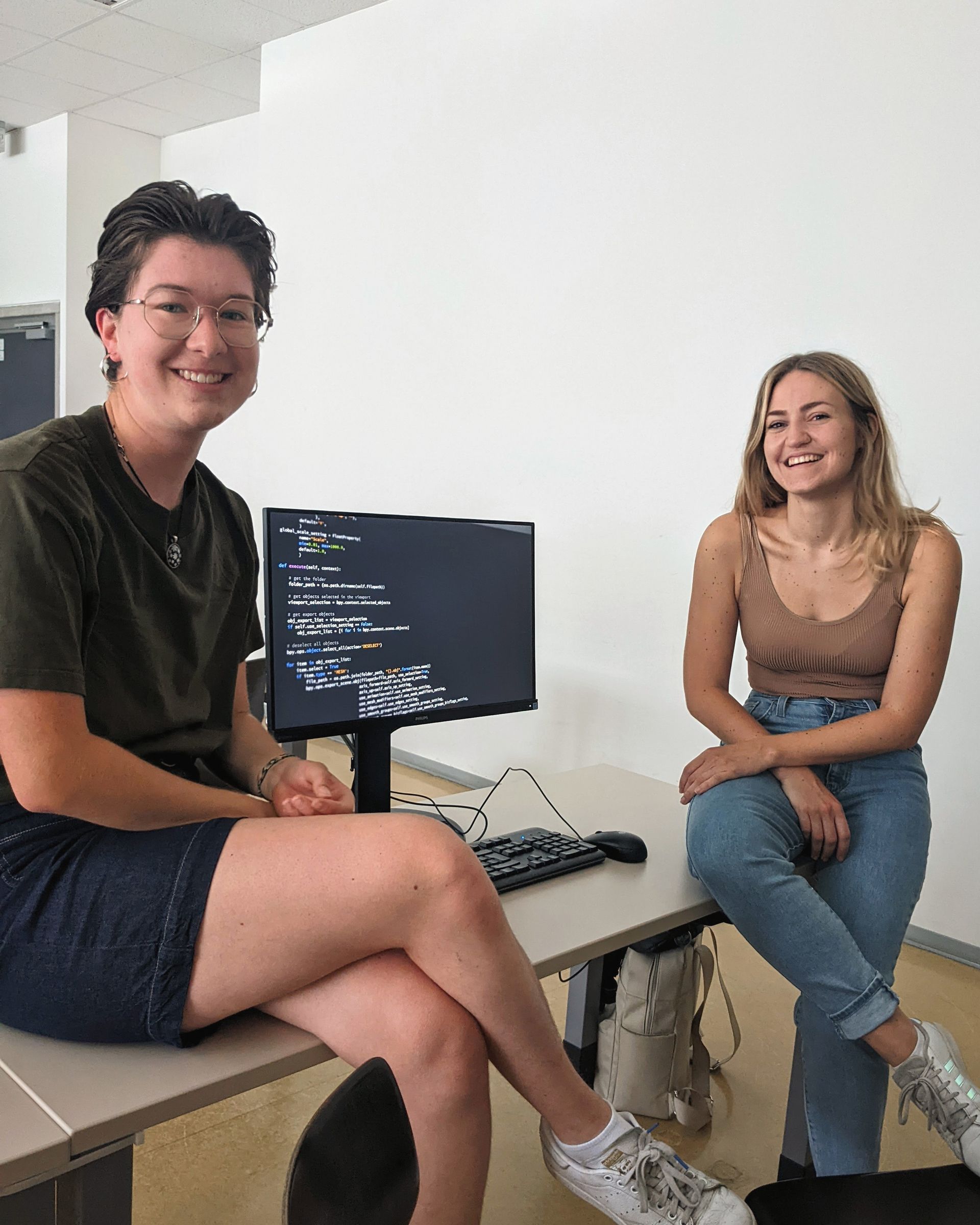 Zwei Informatik-Studentinnen sitzen auf einem Tisch vor einem Computer.