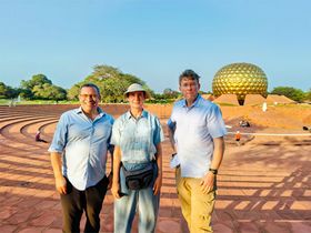 Zwei Männer und eine Frau stehen vor einem Gebäude in Auroville