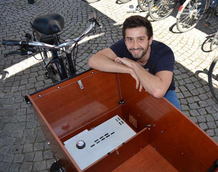 Michael Steinherr kniend hinter einem Lastenfahrrad. Er hat die Arme verschränkt auf die Transportbox gelegt.