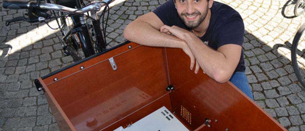 Michael Steinherr kniend hinter einem Lastenfahrrad. Er hat die Arme verschränkt auf die Transportbox gelegt.