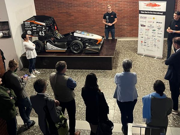 Eine Gruppe Menschen steht im Halbkreis um ein Rennfahrzeug.