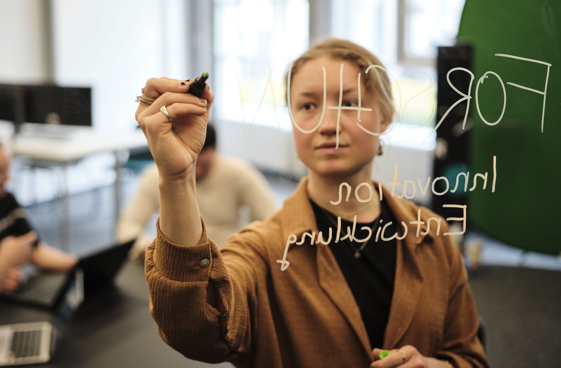 Eine Studentin steht vor einer Gruppe und schreibt auf ein Whiteboard