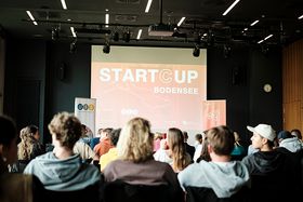 Das Foto zeigt eine Gruppe von Besuchern des Pitches, sie sitzen mit dem Rücken zur Kamera und schauen auf eine Leinwand mit dem Titel der Veranstaltung.