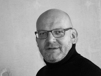 Schwarz-Weiß-Bild von Stephan Grüninger mit Glatze, Brille und schwarzen Pullover.